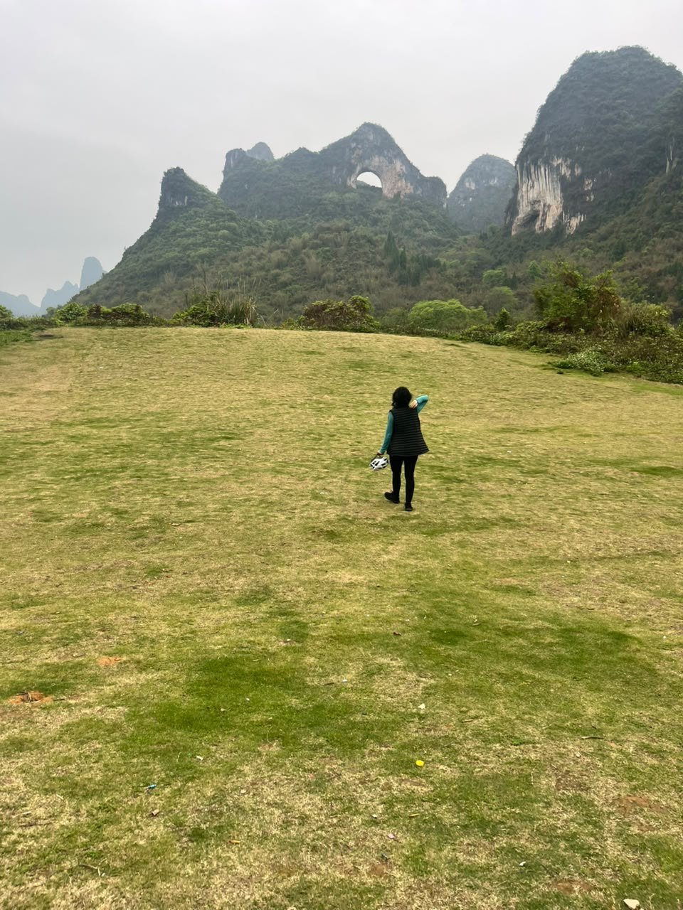 Pessoa caminhando sozinha por um campo aberto diante de montanhas cársticas