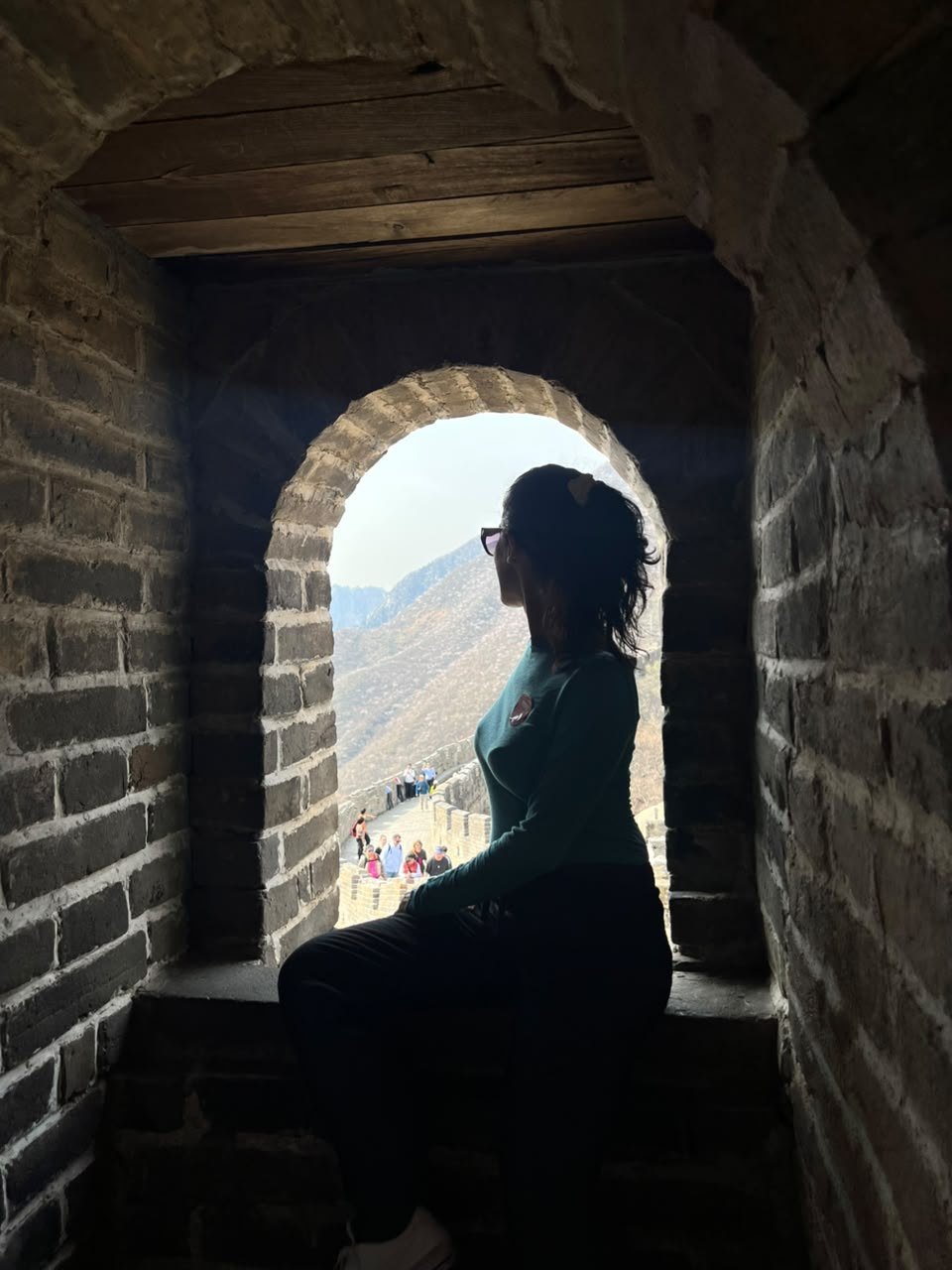 Pessoa sentada na abertura de uma torre de pedra, olhando a montanha lá fora